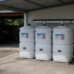 Een installatie van drie witte, bovengrondse mazouttank dubbelwandig modellen die met elkaar verbonden zijn en op een betonnen vloer onder een carport staan.