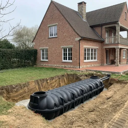Een zeer grote regenwaterput van 20000 liter in kunststof geplaatst in een diepe open put in de grond naast een residentiële woning.